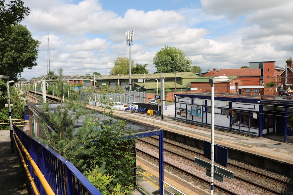 A high-angle view of a railway station platform in daytime showing multiple sets of train tracks extending into the distance, with a small brick and metal shelter with a flat roof on the left side, pa