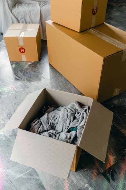 Close-up image of three cardboard moving boxes stacked indoors, with the top box labeled 'STUFF' and a simple smiley face drawn underneath, and the lower box labeled 'CLOTHES' in handwritten black mar
